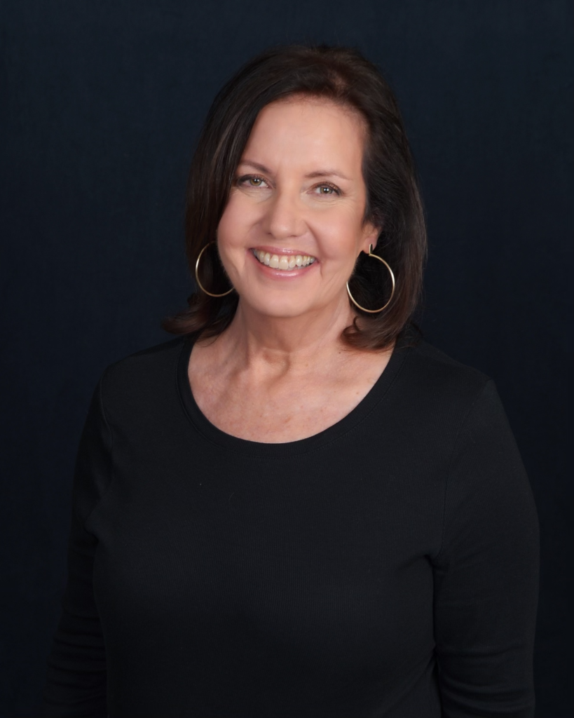 Headshot of Debra Schlact, with a black background. Debra is in a black shirt with gold hoop earrings.